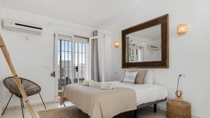 A bedroom with a bed, a large mirror, a standing lamp, and a wicker chair. - Casa Blanca | private pool - garden - bbq (Estepona)