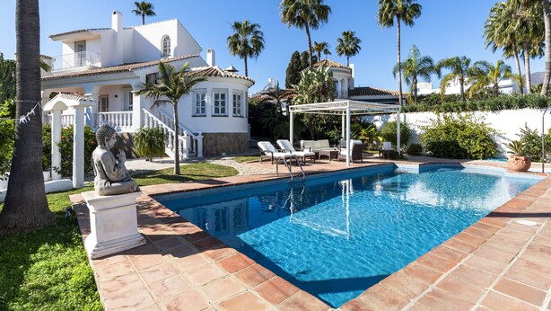 A swimming pool with a pergola and lounge chairs, surrounded by palm trees and a white house with a stone facade. - Casa Blanca | private pool - garden - bbq (Estepona)
