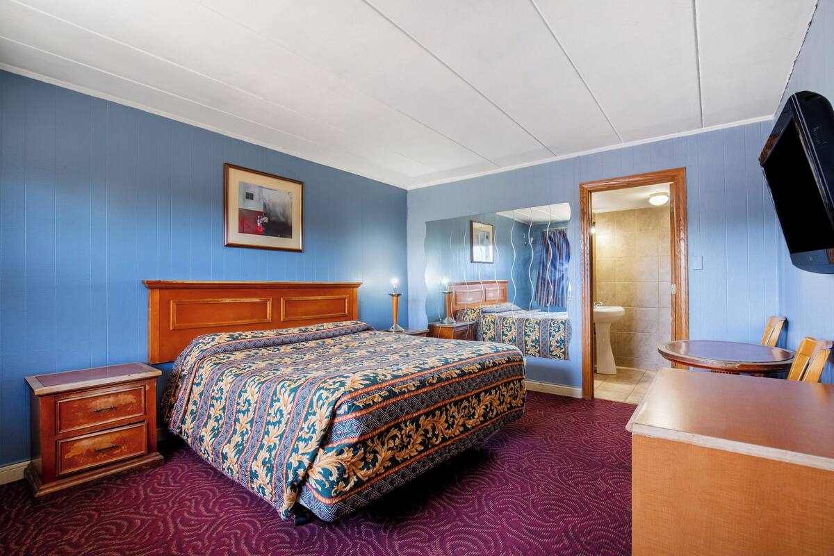 Quarto de hotel com uma cama grande, cômoda de madeira, escrivaninha e um espelho.