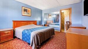 A hotel room with a bed, a dresser, a desk, and a mirror.
