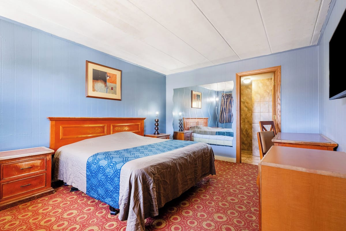 Quarto de hotel com uma cama, cômoda, escrivaninha e espelho.