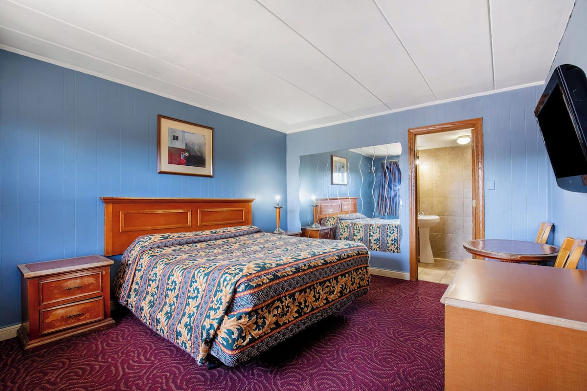 Quarto de hotel com uma cama grande, cômoda de madeira, escrivaninha e um espelho.