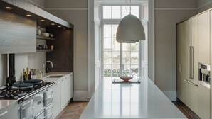Une cuisine moderne dotée d’un îlot central, d’appareils électroménagers intégrés et d’une grande fenêtre qui laisse entrer la lumière naturelle.