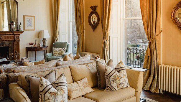 Un salon chaleureux avec un canapé beige, une cheminée, un lustre et une vue sur un balcon.