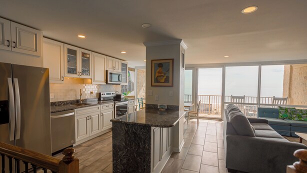 A modern kitchen with white cabinets, a marble island, and a dining area with a gray sofa and a balcony with a view.