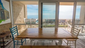 A dining area with a wooden table and chairs, large windows with a view of the sea, and a textured wall.