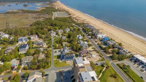An aerial view of a coastal residential area with houses, a beach, and a road.