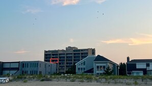 A coastal building complex with multiple floors, a flat roof, and a sandy foreground.