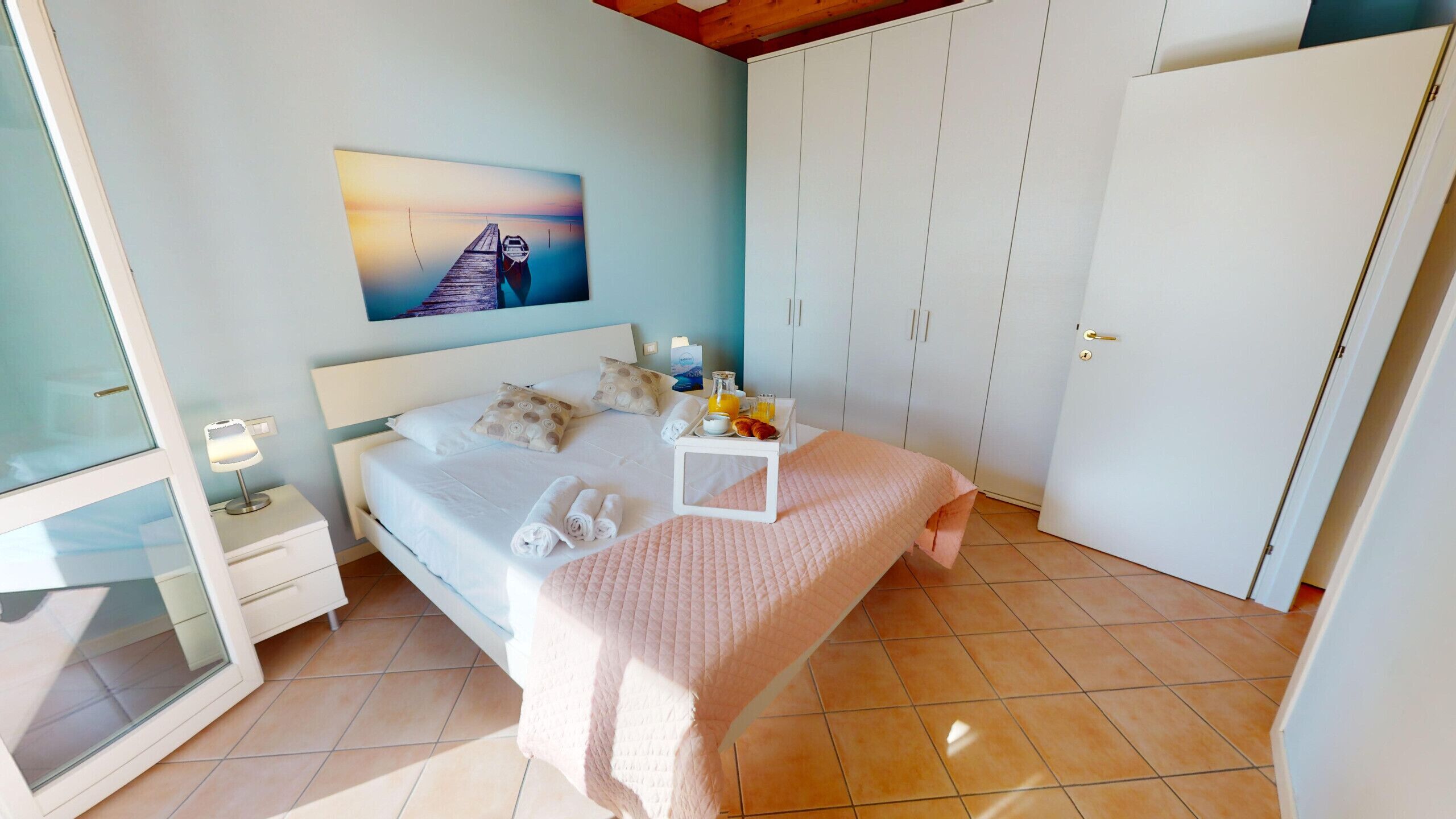 A bedroom with a bed, bedside table, nightstand, wardrobe, and a painting on the wall.