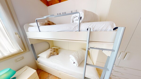 A bunk bed room with a window, a small table, and a wardrobe.