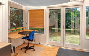 A corner room with a desk, chair, and a view through a glass door to a garden.
