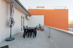 Ein Balkon mit Tisch, Stühlen, einer Topfpflanze und einem Sonnenschirm.