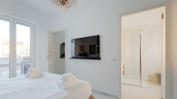 Ein modernes Hotelzimmer mit einem großen Bett, einem an der Wand montierten Fernseher und einem durch eine offene Tür einsehbaren Badezimmer.