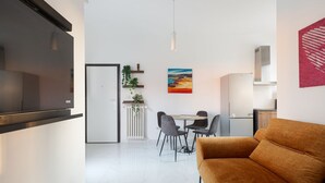 Ein modernes Wohnzimmer mit einer Couch, einem Essbereich mit Stühlen, einer Küche mit Geräten und einem Bild an der Wand.