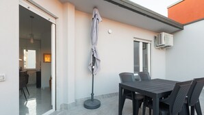 Ein Außenbereich zum Essen mit Tisch und Stühlen, einem schattenspendenden Sonnenschirm und einer Klimaanlage.