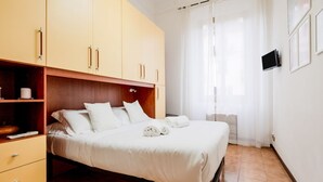 Un dormitorio con cama, armario, televisor y ventana con cortinas.
