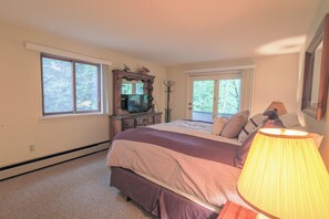 Un dormitorio con cama, cómoda, televisor y ventanas.