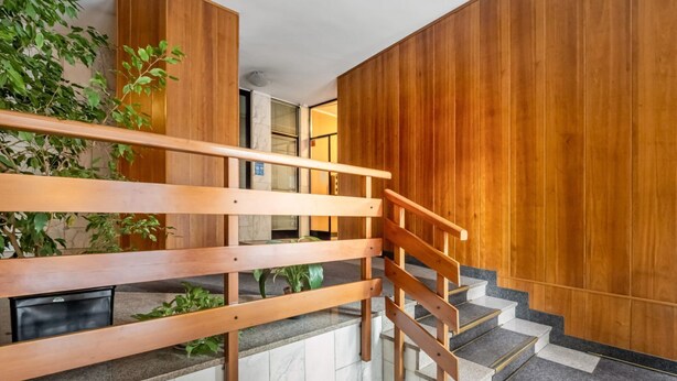 Eine Holztreppe mit Handlauf, Marmorstufen und einer Pflanze links.