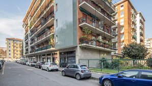 Ein mehrstöckiges Wohnhaus mit Balkonen, parkierten Autos und blauem Himmel.
