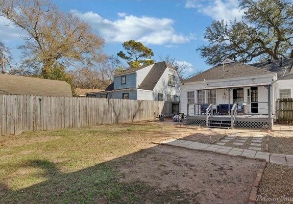 A residential backyard with a wooden fence, a grassy lawn, and a paved patio area.