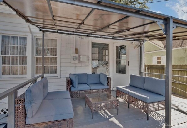 A covered patio with wicker furniture and a glass table.