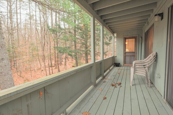 A covered porch with a view of a forest, a bench, and a door leading inside.