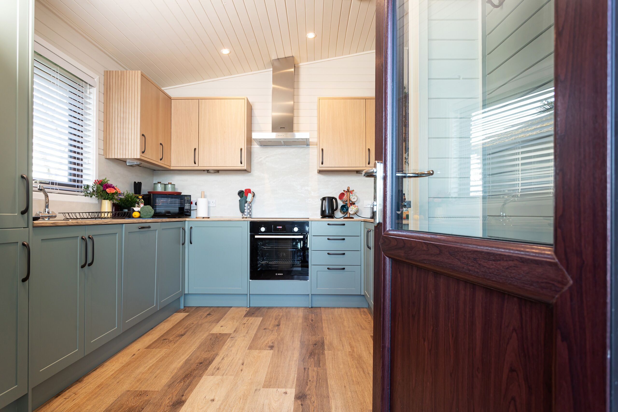 Une cuisine moderne avec des meubles de couleur bleu clair, un plancher en bois et un four encastré.