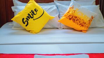 A bed with white bedding and two decorative pillows, one with a smiley face and the other with a floral design.