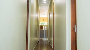 Un pasillo largo y estrecho con suelos de madera y paredes blancas que conduce a una habitación donde se puede ver un área de cocina a lo lejos.