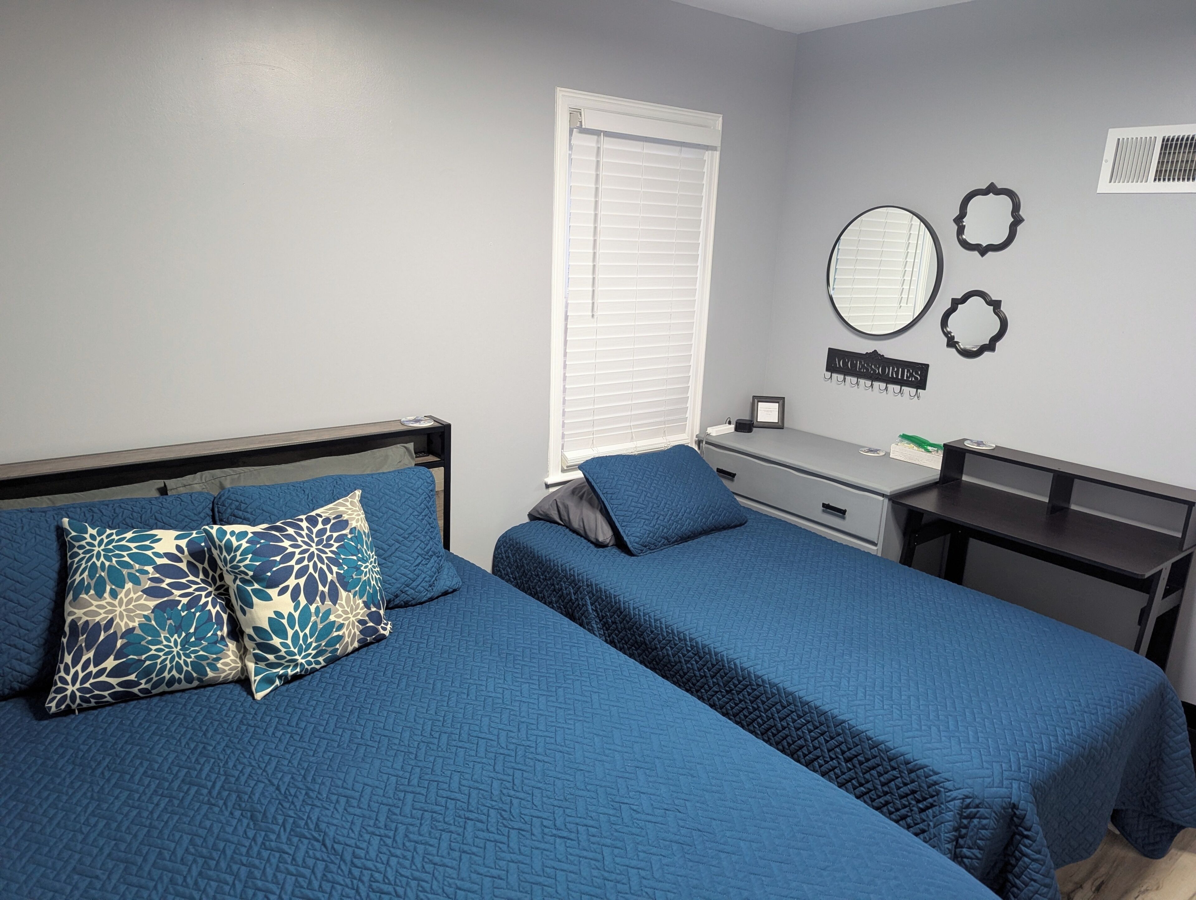 A bedroom with two beds, a dresser, a mirror, and a wall-mounted shelf.
