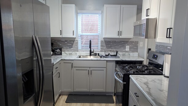 A modern kitchen with stainless steel appliances, white cabinetry, and a large window providing natural light.