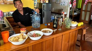 A kitchen counter with various food items, a large water bottle, a bottle of champagne, and a glass of wine. - Finca Beach House (Placencia)