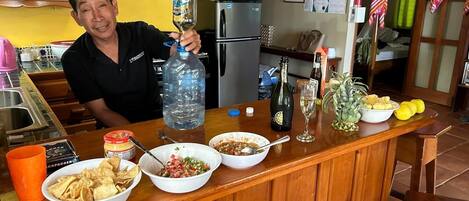 A kitchen counter with various food items, a large water bottle, a bottle of champagne, and a glass of wine.