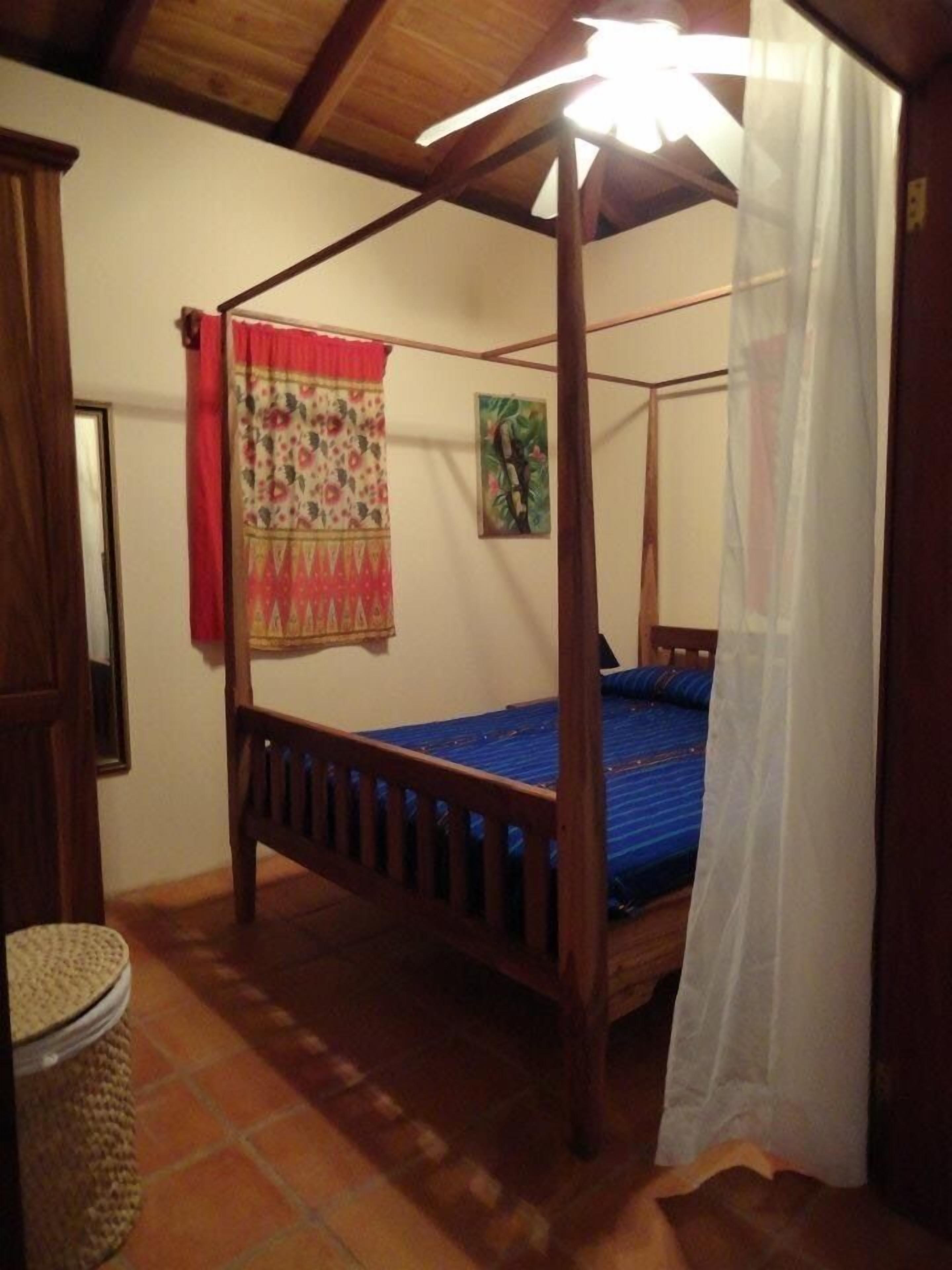 Uma cama com dossel, colchão azul, cabeceira de madeira e toldo branco.