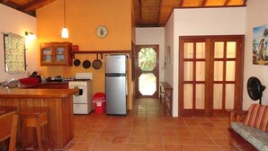 A cozy kitchen with wooden cabinets, a stove, and a refrigerator. There is a dining area with a bench and a sofa. - Finca Beach House (Placencia)