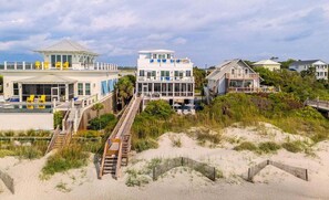 Eine Strandimmobilie mit mehreren Häusern, einem Pool und einer Holzterrasse, die zum Strand führt.