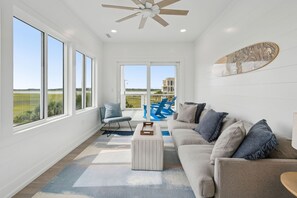Amplia sala de estar con ventanas grandes, ventilador de techo y vistas al exterior.