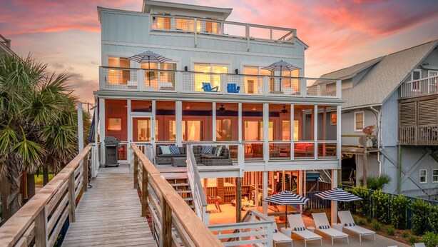 A two-story waterfront property with a deck, outdoor seating, and a pool.