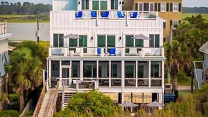 A multi-story beachfront property with a wooden deck, a staircase, and a view of the ocean.