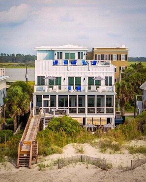 A multi-story beachfront property with a wooden deck, a staircase, and a view of the ocean.