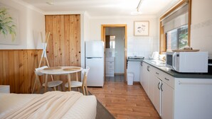 A compact room with a bed, a small dining table with chairs, a kitchenette with a microwave, and a refrigerator. - Sea Shells Studio @ The Blue Seas (Scamander)