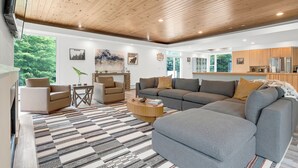 Una sala de estar moderna con un amplio sofá seccional gris, un sillón color beige, una mesa de centro de madera y una alfombra estampada.
