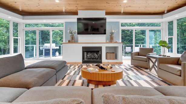 Un salón amplio con un televisor grande, asientos cómodos, una chimenea y ventanas grandes que ofrecen vistas al exterior.