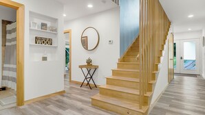 Un interior moderno con una escalera de madera, un espejo y una estantería con objetos decorativos.