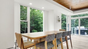 Un comedor moderno con una mesa y sillas de madera, ventanas amplias y vistas al exterior.