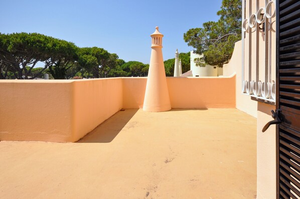 Una terraza en la azotea con un muro color arena, una estructura cónica y una reja metálica.