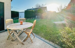 An outdoor patio with a round table and four chairs, surrounded by a grassy yard and a metal fence. - 2 bedroom pet friendly home in Westende (Westende)