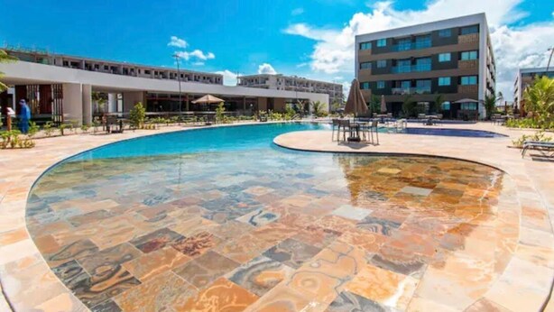 A hotel pool with a unique tile design, surrounded by lounge chairs and umbrellas, with a modern building in the background. - Mana Beach Experience B 114 Muro Alto (Ipojuca)