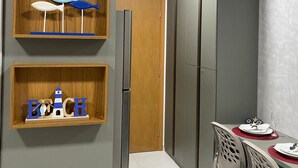 A modern kitchen with built-in cabinets, a refrigerator, and a dining area with a table and chairs. - Mana Beach Experience B 114 Muro Alto (Ipojuca)