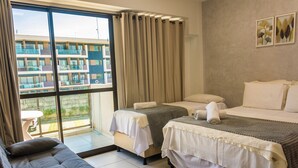 A hotel room with two beds, a sofa, and a balcony with a view of a building. - Mana Beach Experience B 114 Muro Alto (Ipojuca)